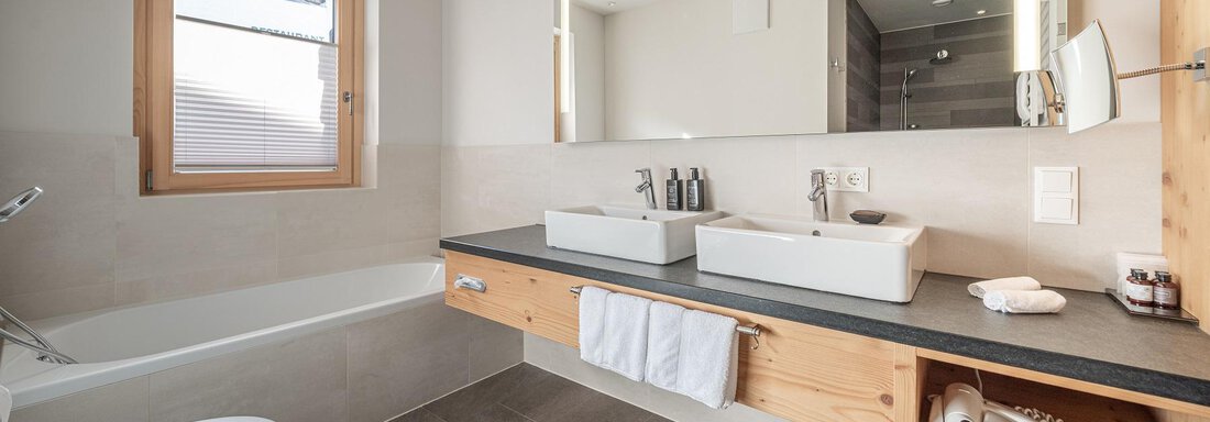 A modern bathroom with a bathtub and two sinks. Large windows provide plenty of daylight and a bright atmosphere. - Gletscherblick - Serviced Apartments - Obergurgl 