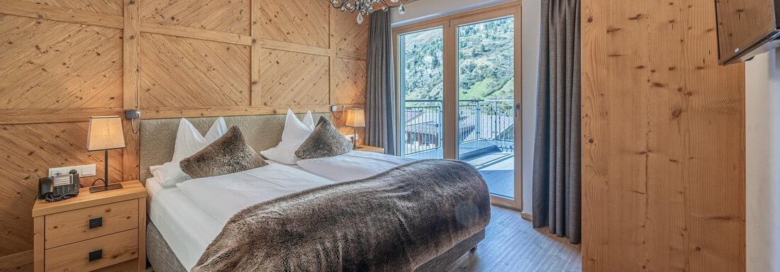 Apt_11_SZ A cozy bedroom with a double bed and wooden walls. Large windows offer a beautiful view and provide plenty of daylight. - Gletscherblick - Serviced Apartments - Obergurgl