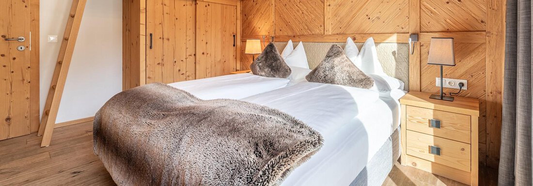 A cozy bedroom with wood paneling and a double bed. There is a functional wardrobe and a dresser next to the bed. - Gletscherblick - Serviced Apartments - Obergurgl 