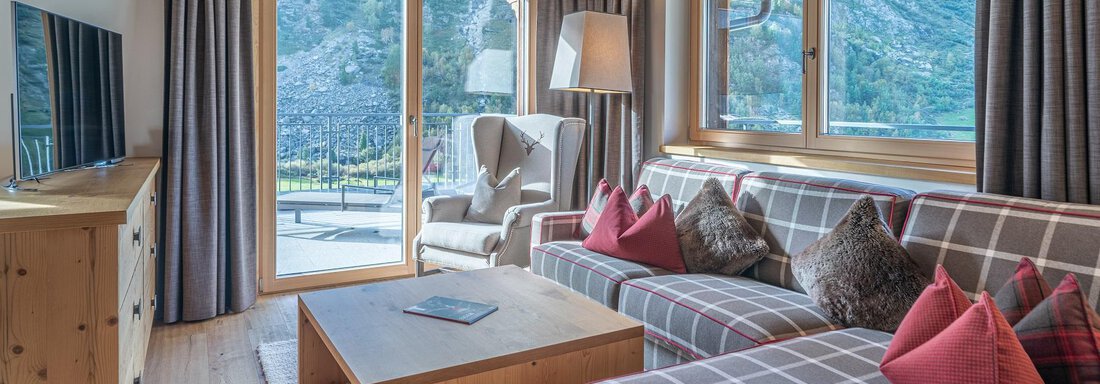 A cozy living room with a modern sofa and large windows. The room has wooden details and is bright and inviting. - Gletscherblick - Serviced Apartments - Obergurgl 