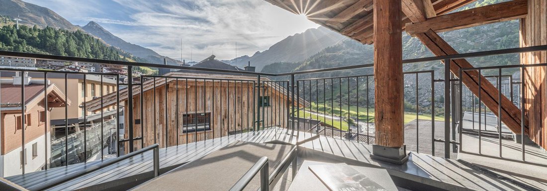 A cozy terrace with a sun lounger and table, surrounded by a picturesque mountain landscape. The sun shines through the clouds, creating an inviting atmosphere. - Gletscherblick - Serviced Apartments - Obergurgl 
