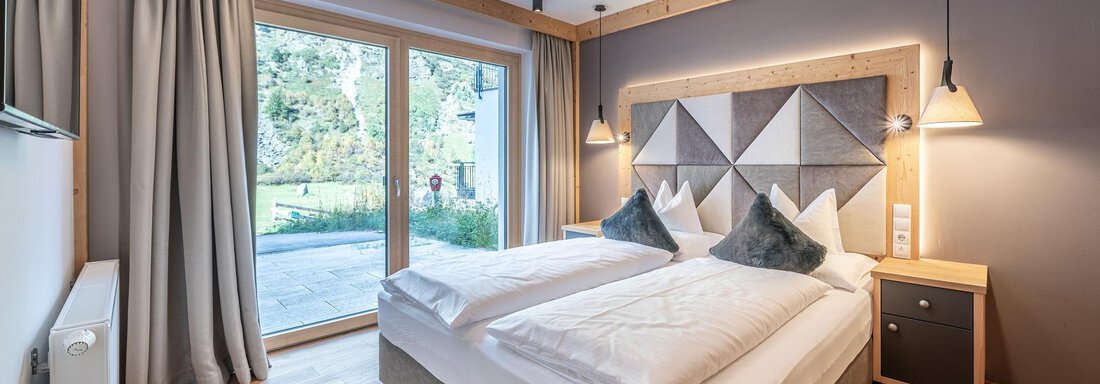 Apt_21_SZ A modern bedroom with two single beds and a cozy wood design. Large windows provide plenty of daylight and a view of the outdoors. - Gletscherblick - Serviced Apartments - Obergurgl