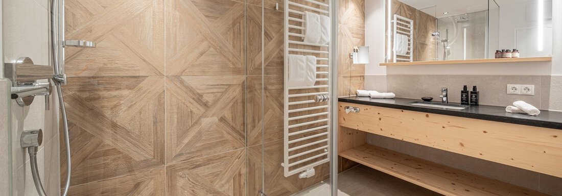 A modern bathroom with a glass shower cubicle and wooden elements. The area is brightly lit and stylishly furnished. - Gletscherblick - Serviced Apartments - Obergurgl 