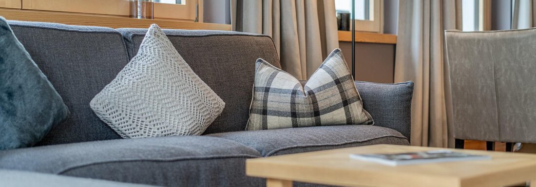 A cozy living room with a gray sofa and several cushions. A small table and a floor lamp complement the decor. - Gletscherblick - Serviced Apartments - Obergurgl 