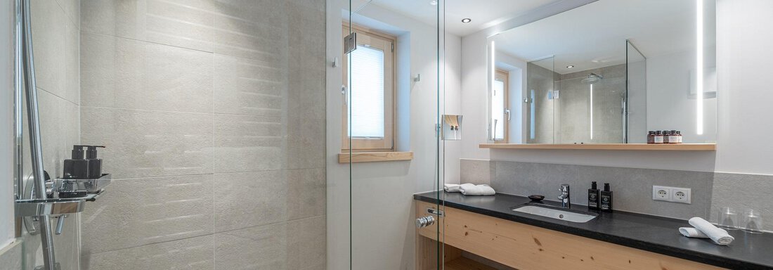 A modern bathroom with a large glass shower and a stylish, bright decor. The wooden vanity and the clear lighting give the space an inviting atmosphere. - Gletscherblick - Serviced Apartments - Obergurgl 