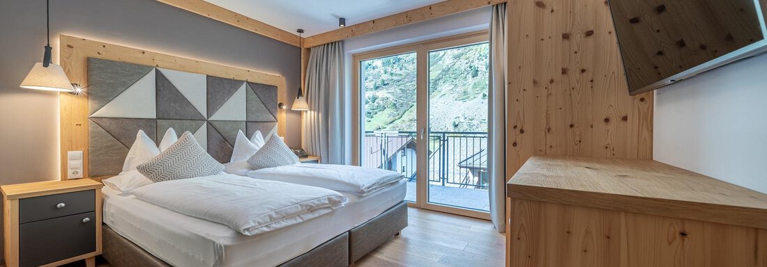 Apt_24_SZ A modern bedroom with two beds and light wooden panels. Large windows offer a view outside. - Gletscherblick - Serviced Apartments - Obergurgl