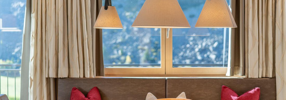 A cozy dining area with a wooden table and comfortable chairs. Decorative lamps hang above the table, and large windows provide plenty of daylight. - Gletscherblick - Serviced Apartments - Obergurgl 