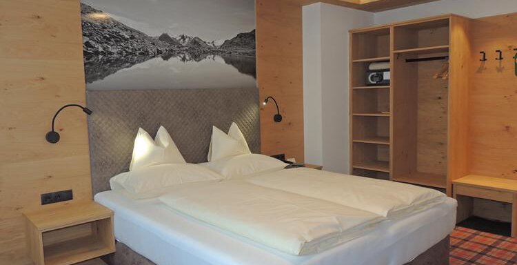 A cozy room with a double bed and wooden paneling. On the wall hangs a picture of a mountain landscape. - Haus Christophorus - Obergurgl 