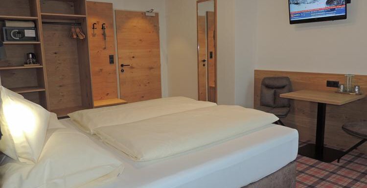 A modern hotel room with a large double bed and a flat-screen TV. There is a table as well as a cozy seating area and a wardrobe. - Haus Christophorus - Obergurgl 