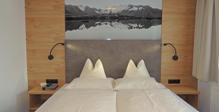 A modern hotel room with two single beds and wood paneling. A black and white landscape painting hangs on the wall. - Haus Christophorus - Obergurgl 