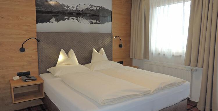 A modern bedroom with a large, comfortable bed and two pillows. The walls are paneled with wood, and a large window provides plenty of daylight. - Haus Christophorus - Obergurgl 