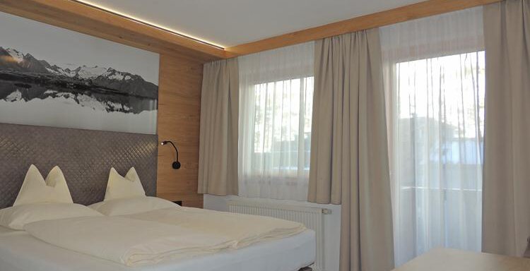 A modern bedroom with a double bed and large windows. The walls are designed in wood look, and a stylish picture is mounted above the bed. - Haus Christophorus - Obergurgl 