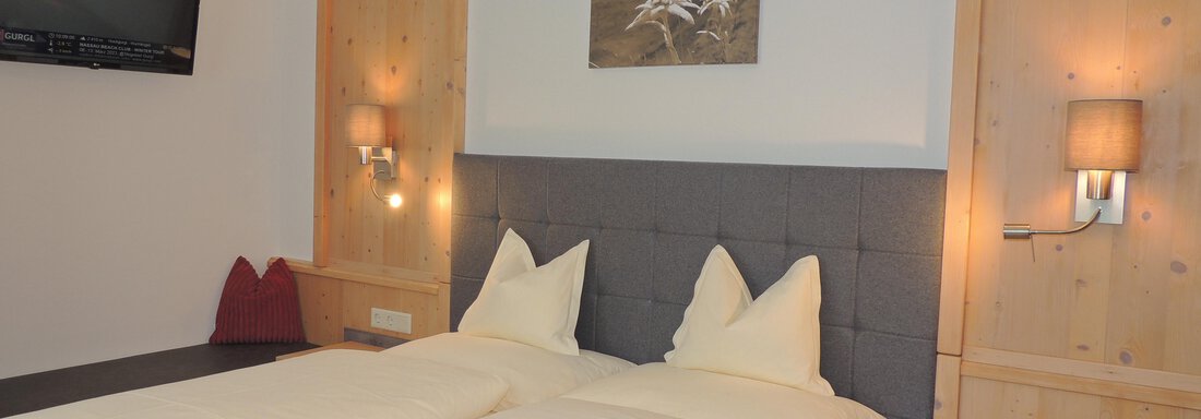 A cozy bedroom with two beds and white bedspreads. The walls are made of wood, and there is a TV as well as a decorative picture above the bed. - Haus Christophorus - Obergurgl 