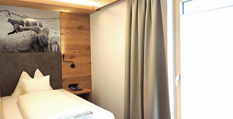 A cozy bedroom with a single bed and wood paneling. A window with curtains lets natural light in. - Haus Christophorus - Obergurgl 