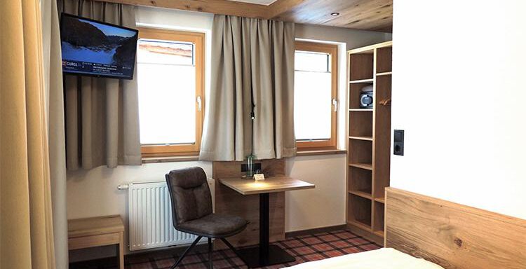 A cozy hotel room with a bed, a table, and a chair. A television hangs on the wall, and the windows are fitted with curtains. - Haus Christophorus - Obergurgl 