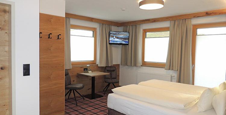 A modern hotel room with two beds, a table, and a television. Large windows provide plenty of daylight. - Haus Christophorus - Obergurgl 