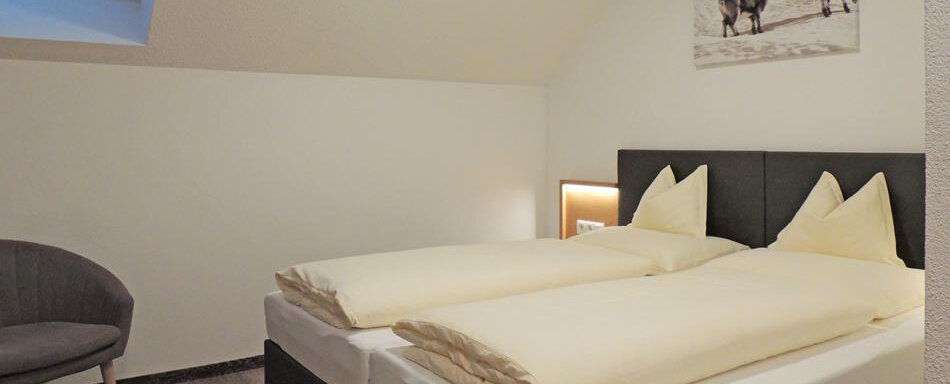 A modern bedroom with two single beds and a cozy seating area. A picture of horses hangs on the wall. - Haus Christophorus - Obergurgl 