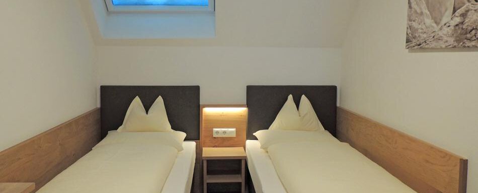 A cozy room with two single beds and a window. The walls are painted in neutral colors and the furnishings are modern. - Haus Christophorus - Obergurgl 