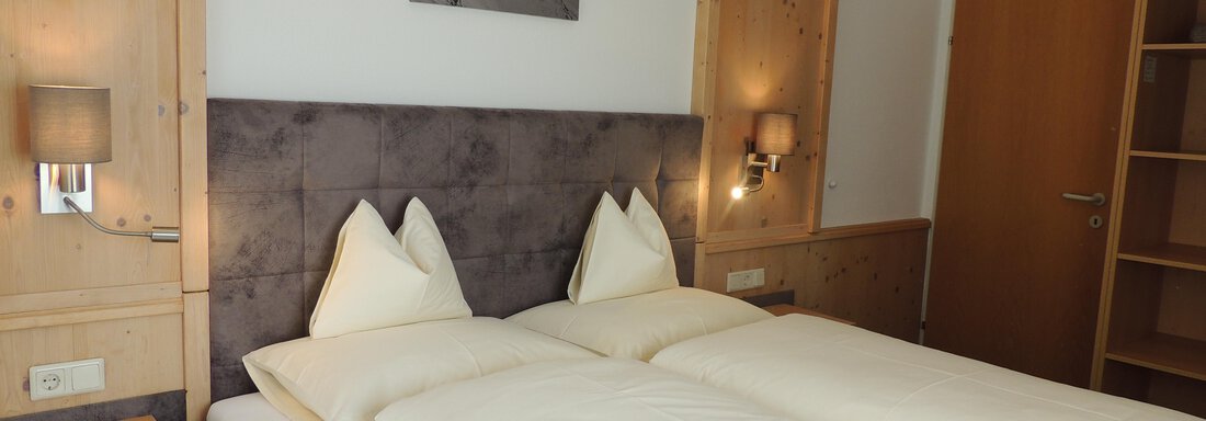 A cozy bedroom with two beds and wood-paneled walls. The decor is simple and modern, with a picture on the wall and an open wardrobe nook. - Haus Christophorus - Obergurgl 