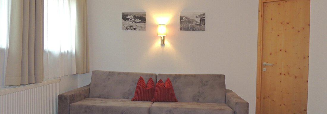 A cozy living room with a gray sofa and red stools. There is a small table and two pictures on the wall. - Haus Christophorus - Obergurgl 