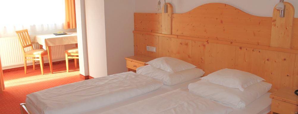 A simple room with two wooden single beds. There is a table and chairs in the corner as well as a large window front. - Haus Martinshof - Obergurgl 