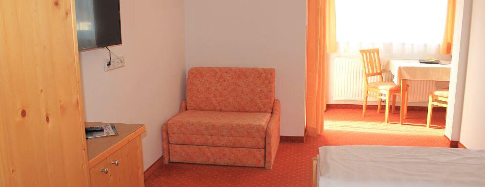 A cozy hotel room with a comfortable sofa and a table. The walls are light, and there is a window with a view of the light. - Haus Martinshof - Obergurgl 