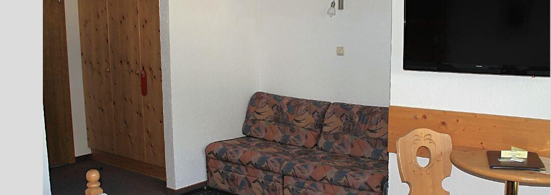 A simple room with two beds, a sofa, and a television. The room also has a wooden wardrobe and a small table. - Haus Martinshof - Obergurgl 