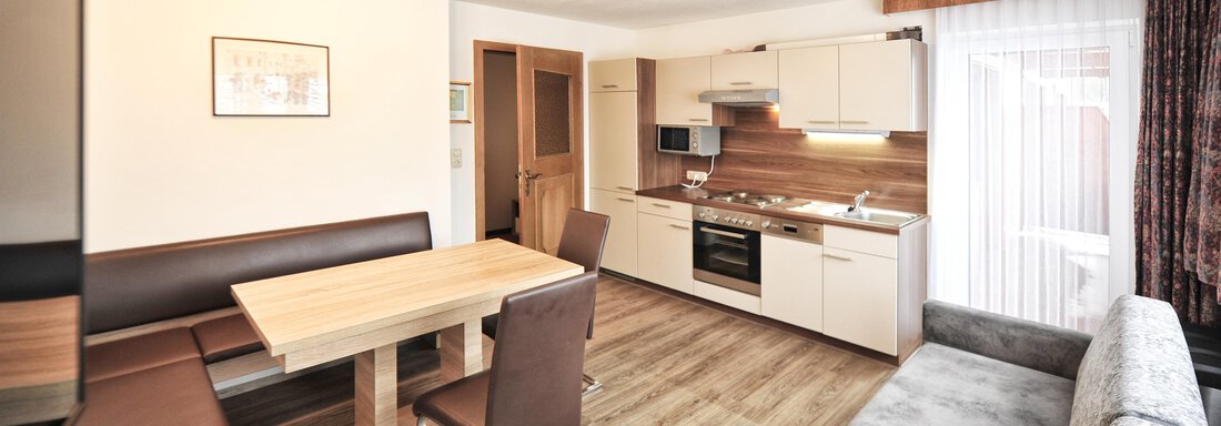 A modern, bright living room with an open kitchen. The room is furnished with a dining table, chairs, and a cozy sofa. - Haus Timmelseck - Obergurgl 