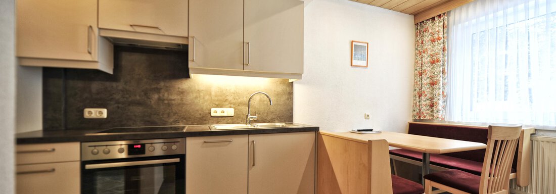 A modern kitchen with a dining table and chairs. There are bright furnishings and ample light from the window. - Haus Timmelseck - Obergurgl 