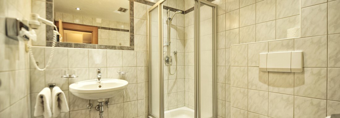 A modern bathroom with tiled walls and a shower. It also includes a sink and a toilet. - Haus Timmelseck - Obergurgl 