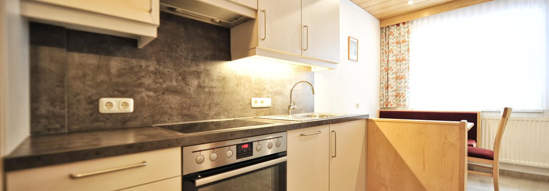 A modern kitchen with bright cabinets and a stone countertop. In the background, there is a dining area with a table and chairs. - Haus Timmelseck - Obergurgl 