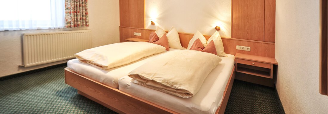 A simple bedroom with a large double bed and two nightstands. The room has bright walls and a cozy atmosphere. - Haus Timmelseck - Obergurgl 