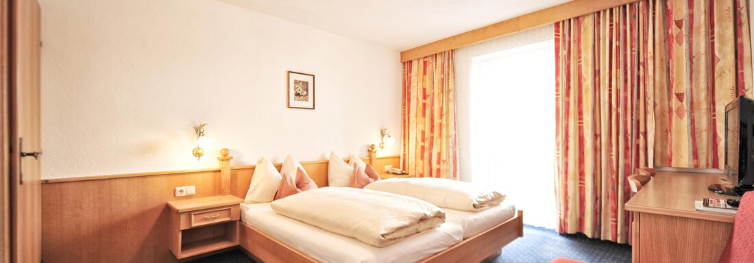 A cozy hotel room with two beds and a red sofa.  
Large windows with curtains create a bright, inviting atmosphere. - Haus Timmelseck - Obergurgl 