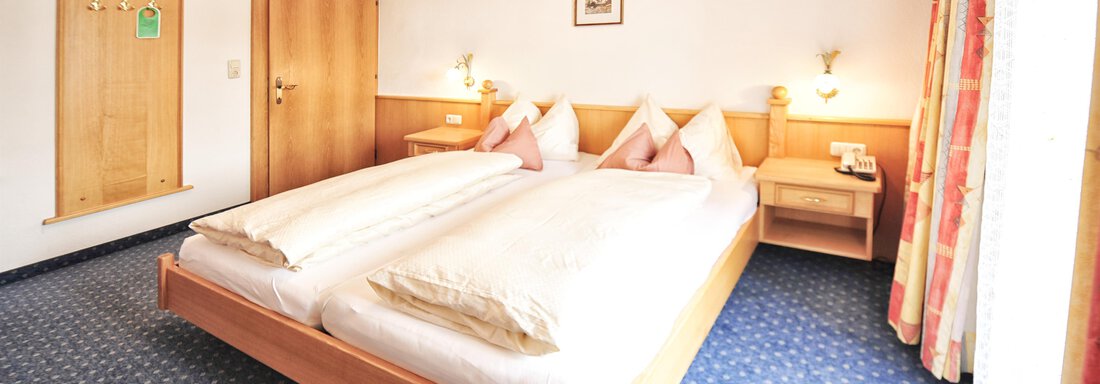A cozy bedroom with two single beds and wooden furniture. The walls are painted light and the carpet is blue. - Haus Timmelseck - Obergurgl 