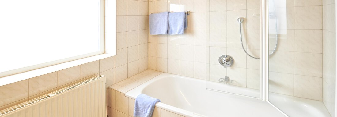 A bright bathroom with a bathtub and a shower. Towels hang on the wall and a window provides natural light. - Haus Timmelseck - Obergurgl 