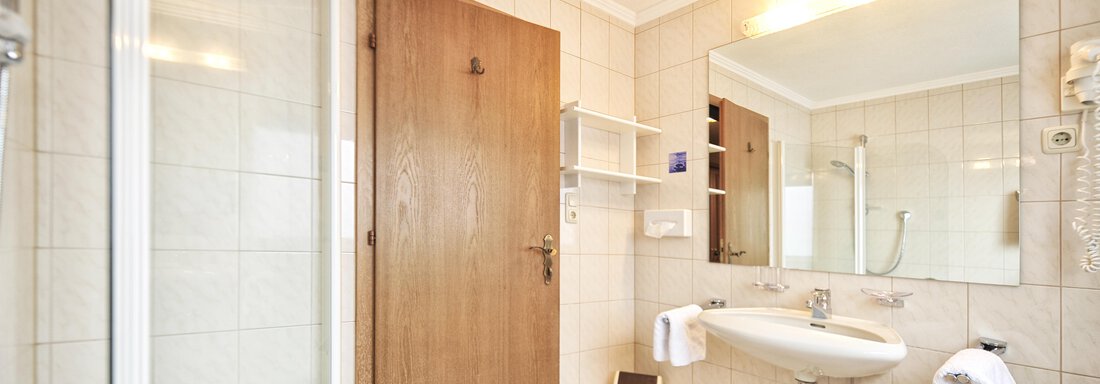 A modern bathroom with a bathtub, shower, and a large mirror. The walls are tiled, and there is a wooden element door. - Haus Timmelseck - Obergurgl 
