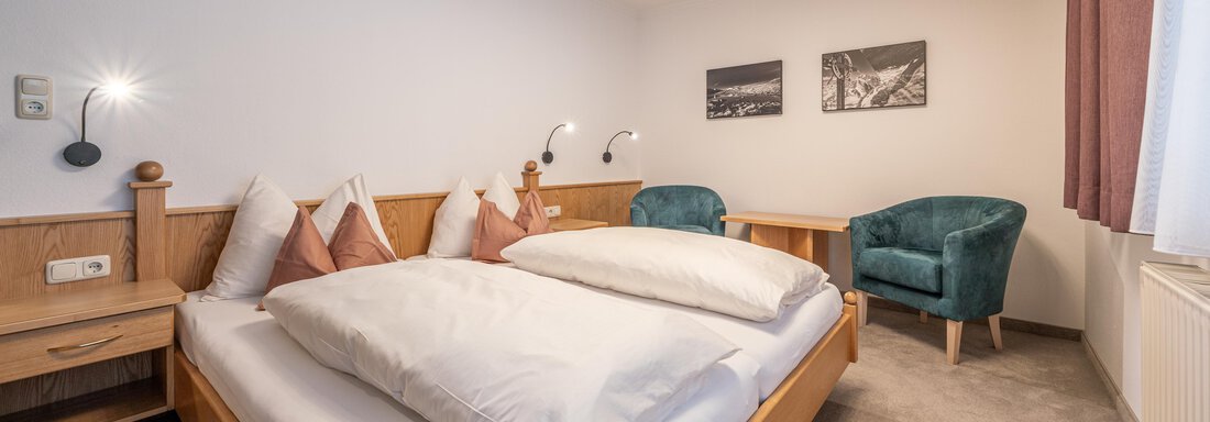 A cozy bedroom with a double bed and stylish cushions. The room features a modern armchair and decorative wall art. - Haus Timmelseck - Obergurgl 