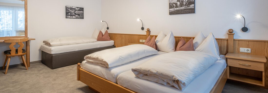 A cozy bedroom with two beds and a single bed. The walls are decorated with wooden paneling and pictures, and there is a table with chairs. - Haus Timmelseck - Obergurgl 