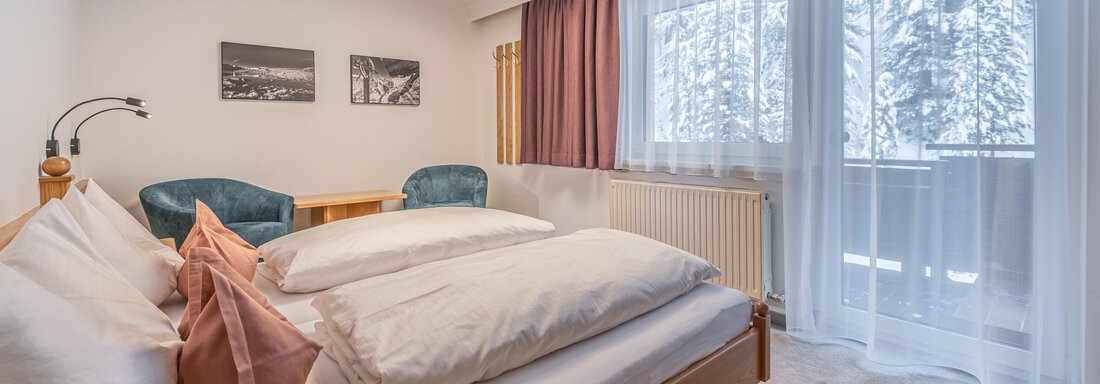 A modern bedroom with a large double bed and comfortable armchairs.  

Large windows let in plenty of light and offer a view of the snowy landscape. - Haus Timmelseck - Obergurgl 