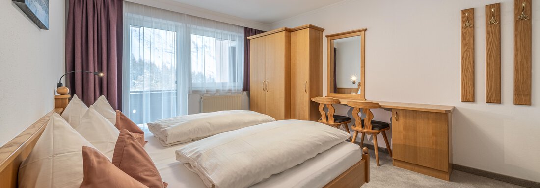A modern bedroom with two beds, wooden furniture, and large windows. The room is bright and pleasantly designed. - Haus Timmelseck - Obergurgl 
