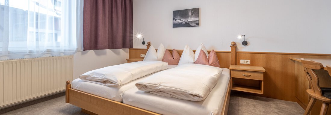 A cozy bedroom with a double bed and bright curtains. The room is simply furnished and offers a clear view of the surroundings. - Haus Timmelseck - Obergurgl 
