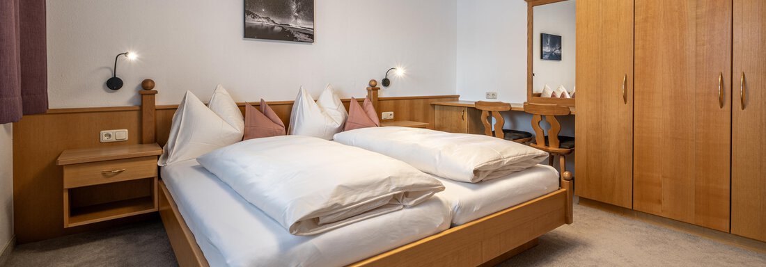 A cozy bedroom with a double bed and wooden furniture. The room features a wardrobe and a mirror. - Haus Timmelseck - Obergurgl 