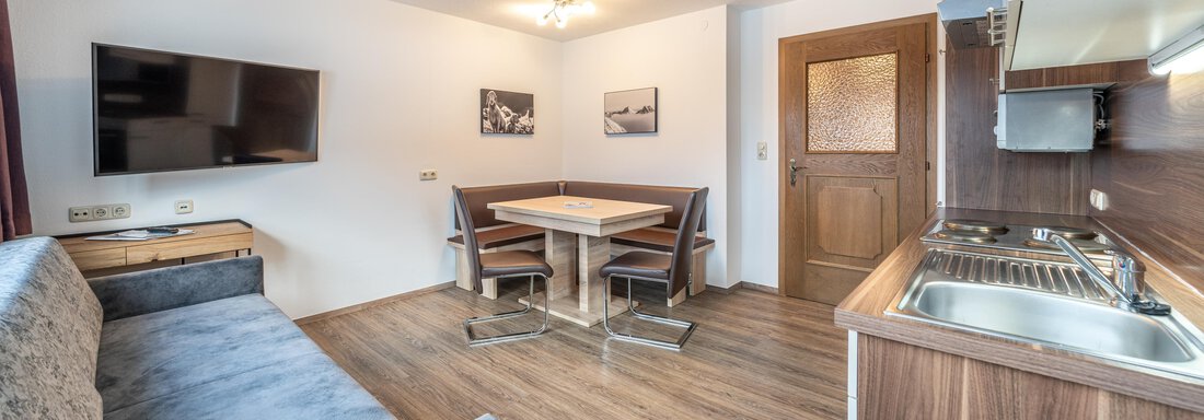 A modern living room with a sofa, a dining table, and chairs. The open kitchen is well-equipped, and the space has a bright, friendly impression. - Haus Timmelseck - Obergurgl 