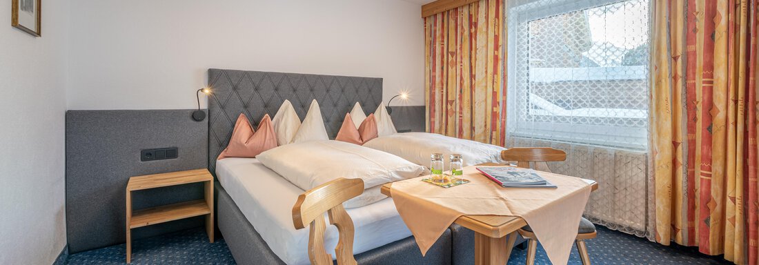 A cozy room with a double bed and a small table. The large windows bring in plenty of daylight. - Haus Timmelseck - Obergurgl 
