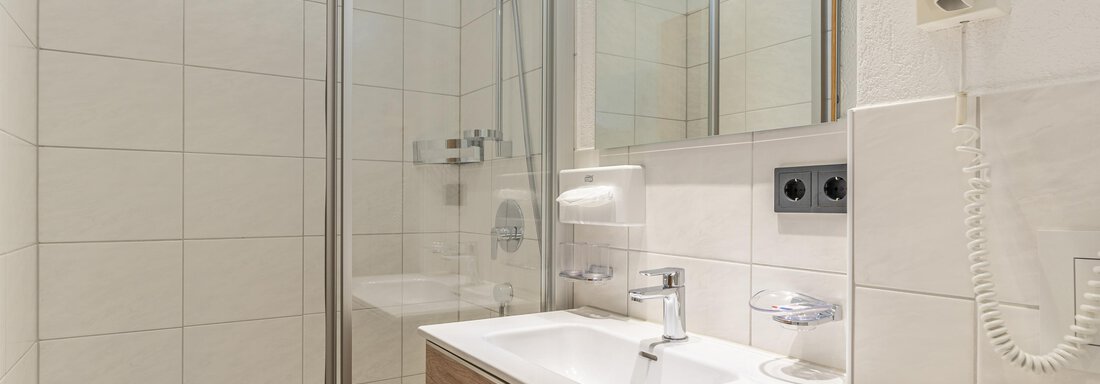 A modern bathroom with a shower and a wooden sink. White tiles and large mirrors create a bright and clean impression. - Haus Timmelseck - Obergurgl 
