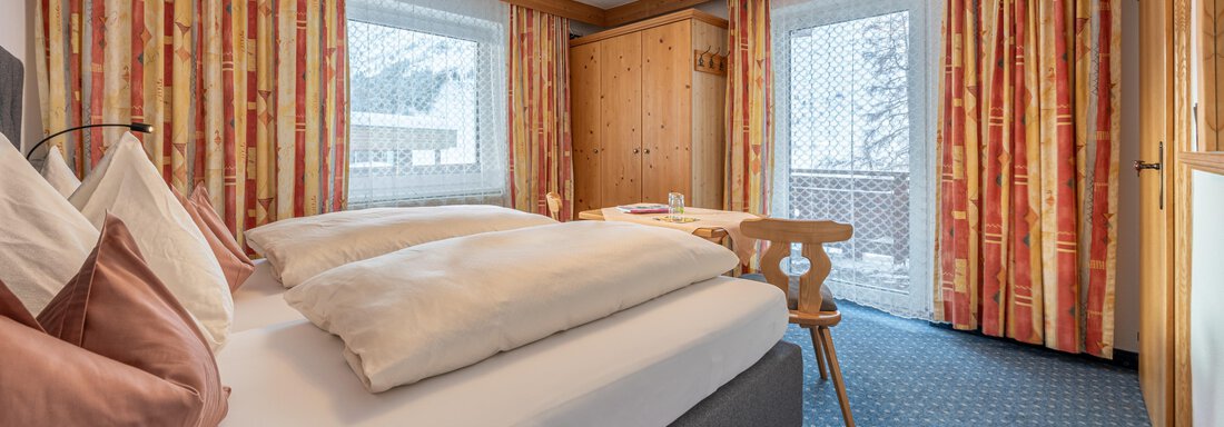 A modern bedroom with a large bed and warm colors. Large windows provide a view of the surroundings and plenty of daylight. - Haus Timmelseck - Obergurgl 