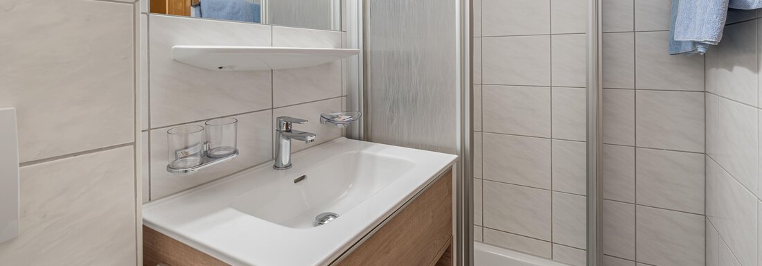A modern bathroom with a shower and a wooden sink. The walls are tiled and there are blue towels. - Haus Timmelseck - Obergurgl 