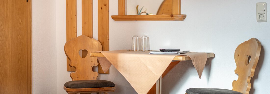 A cozy table with two chairs stands in a bright room. Wooden panels and a mirror hang on the wall. - Haus Timmelseck - Obergurgl 