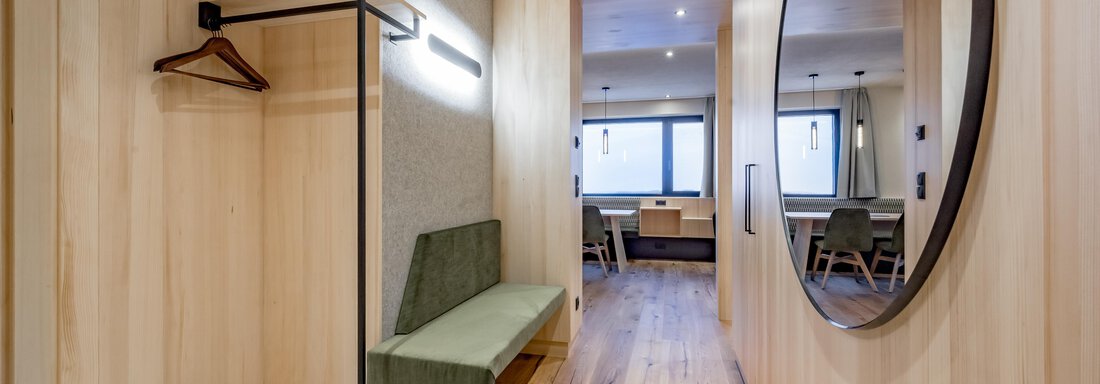 A modern hallway with wood-paneled walls and a large mirror. On the left side, there is a bench and a coat rack. - Hotel-Garni Pirchhütt - Obergurgl 
