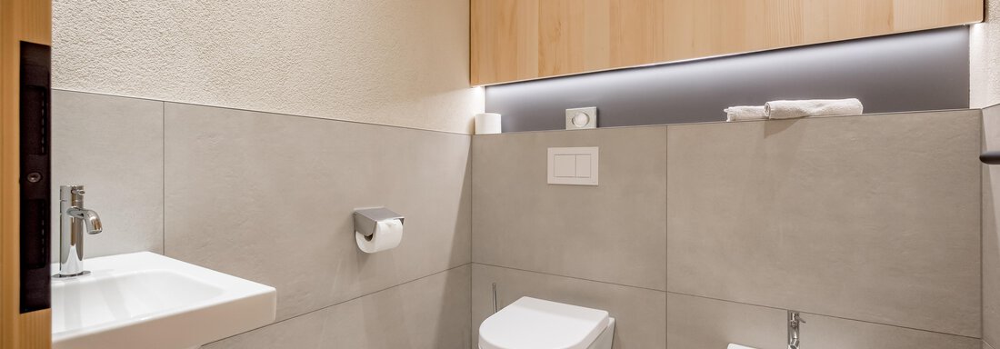 A modern bathroom with gray tiles and light wooden elements. It includes a sink, a toilet, and a bidet. - Hotel-Garni Pirchhütt - Obergurgl 